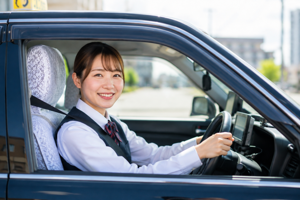 日勤で働く女性タクシードライバーが笑顔で運転する様子。地域の暮らしを支える送迎業務のイメージ